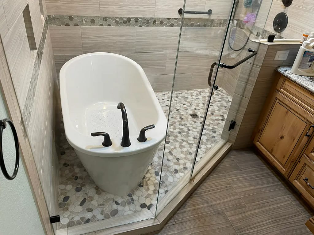 Close-up of a modern freestanding tub and glass shower enclosure in a custom wet room in The Broadmoor featuring textured neutral tiles by XCEL TILE.