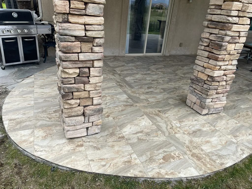 Close-up of large-format outdoor stone-look porcelain patio tiles in Peyton, CO, meeting custom stacked stone support columns by XCEL TILE.