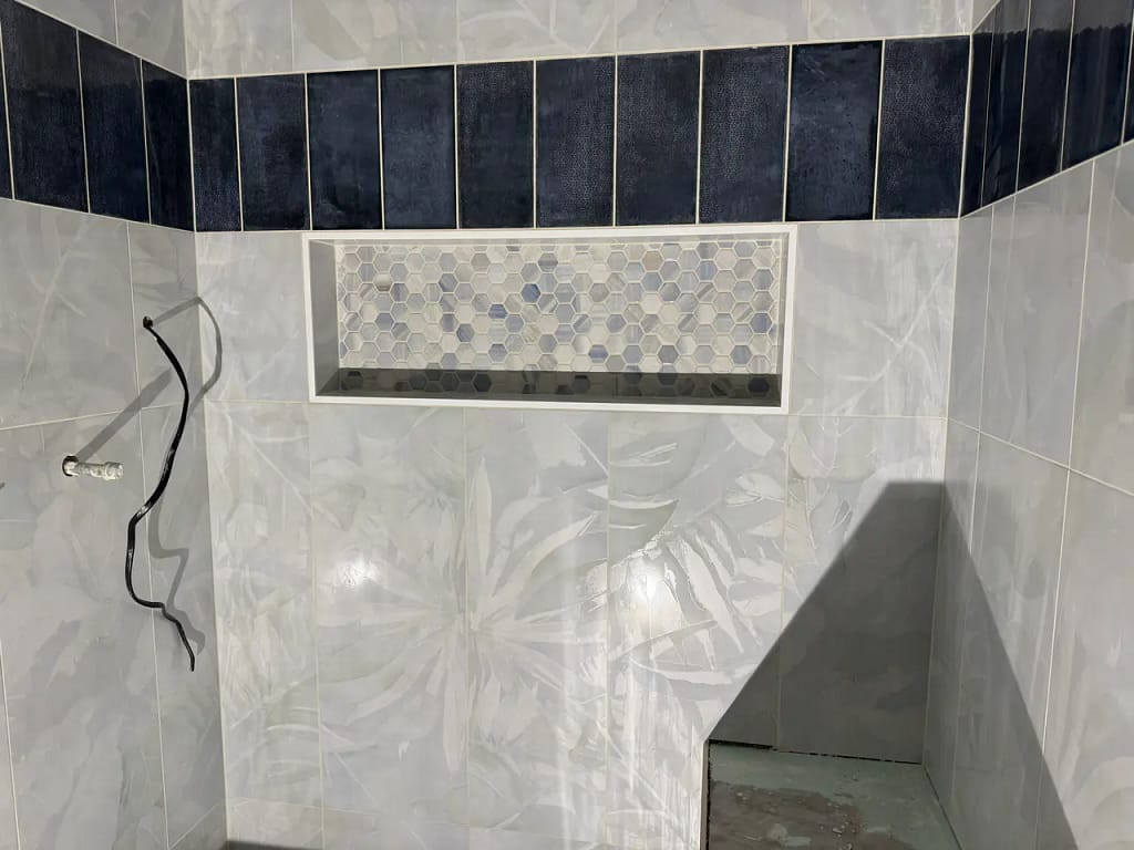 Close-up of a custom wide shower niche filled with hexagon mosaic tiles, positioned seamlessly below a band of dark navy vertical accent tiles in Manitou Springs, CO, by XCEL TILE.