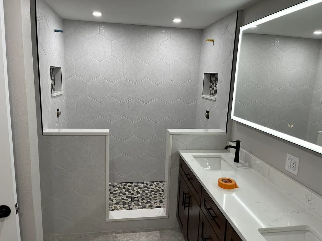 Modern master bathroom in Woodland Park, CO, featuring a walk-in shower with light grey hexagon wall tiles and a pebble mosaic floor by XCEL TILE.