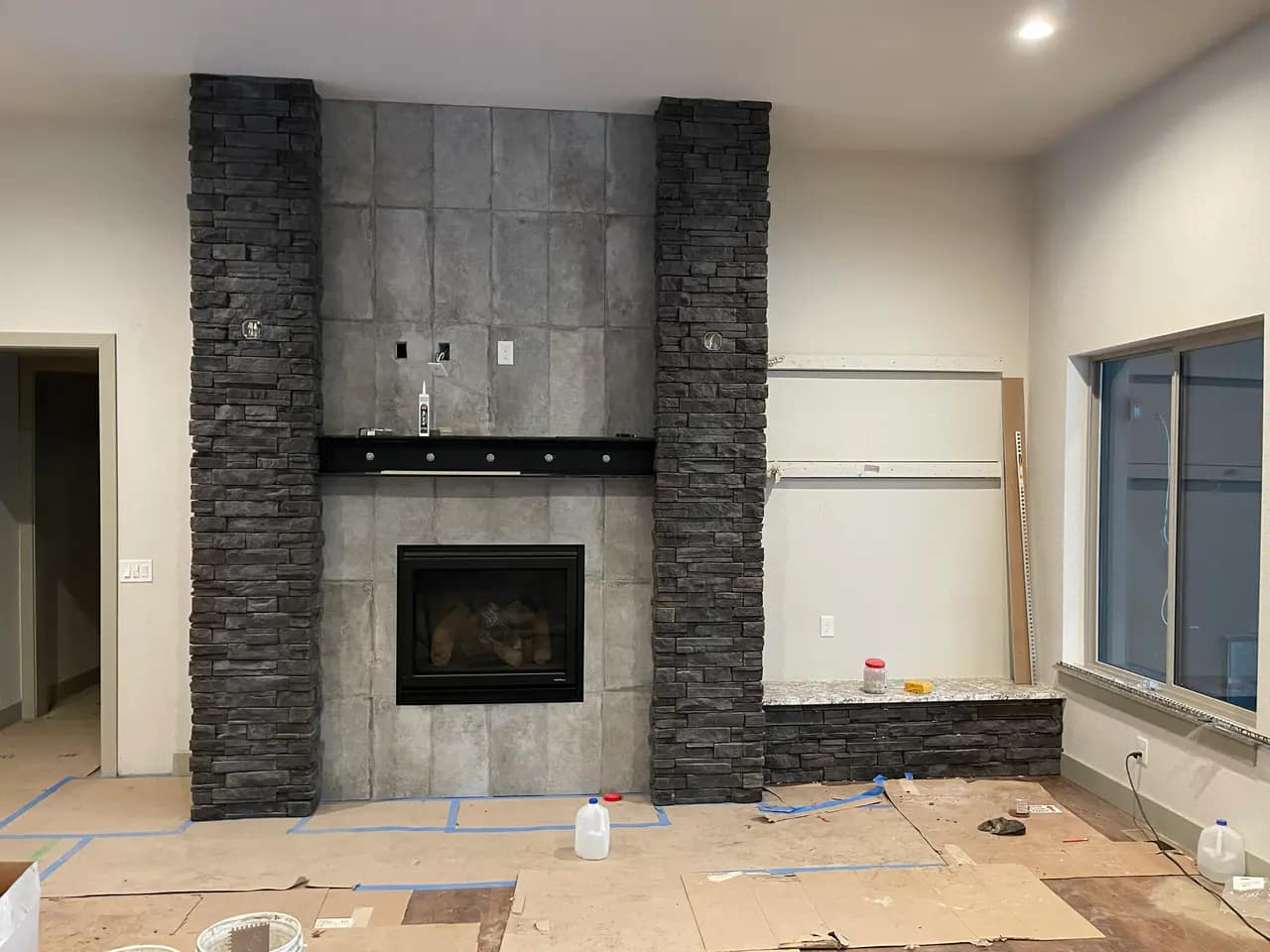 Large custom fireplace under construction, featuring a smooth grey tile center flanked by two floor-to-ceiling columns of dark stacked stone. Custom Stone Fireplaces & Feature Walls Colorado Springs | XCEL TILE