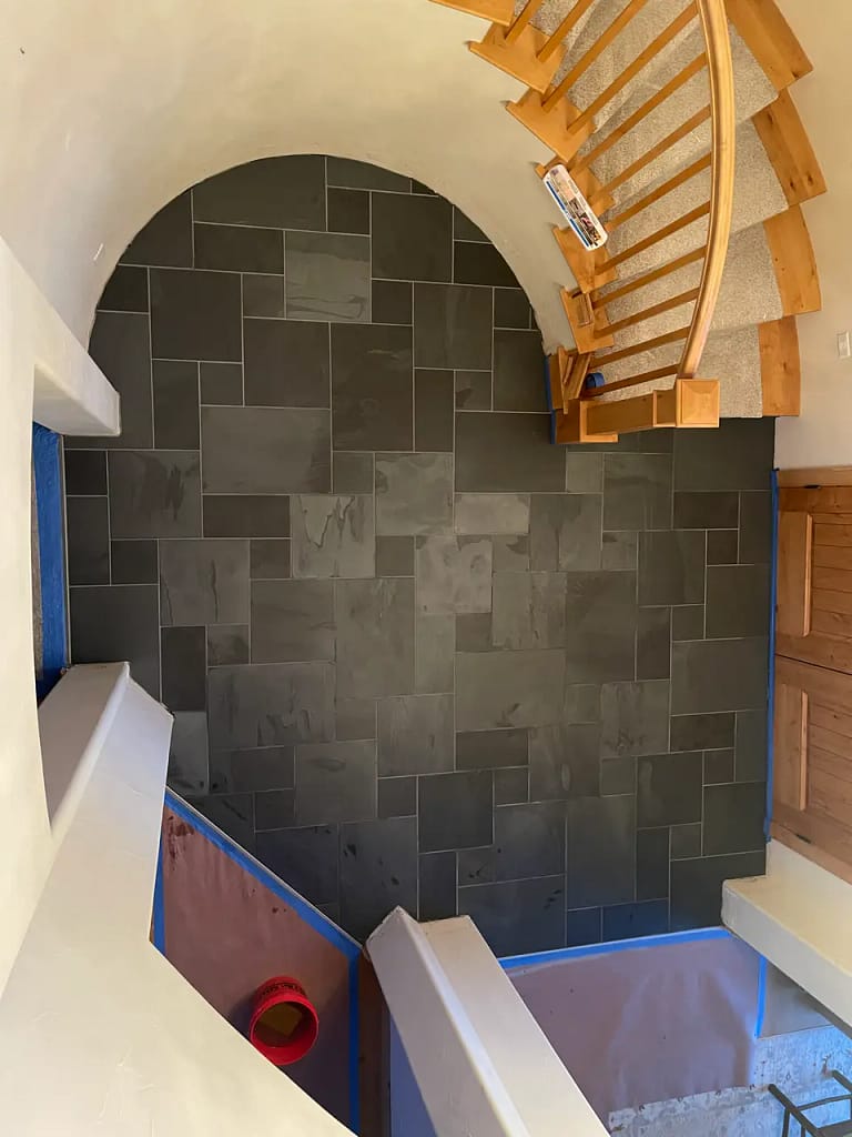Overhead view of a curved entryway floor finished in dark multi-size natural slate tiles featuring precise radius cuts tracing a staircase in Monument, CO, by XCEL TILE.