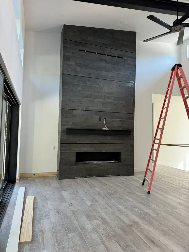 Modern living room in Black Forest, CO, featuring a tall floor-to-ceiling fireplace surround tiled with dark stacked horizontal porcelain planks by XCEL TILE.