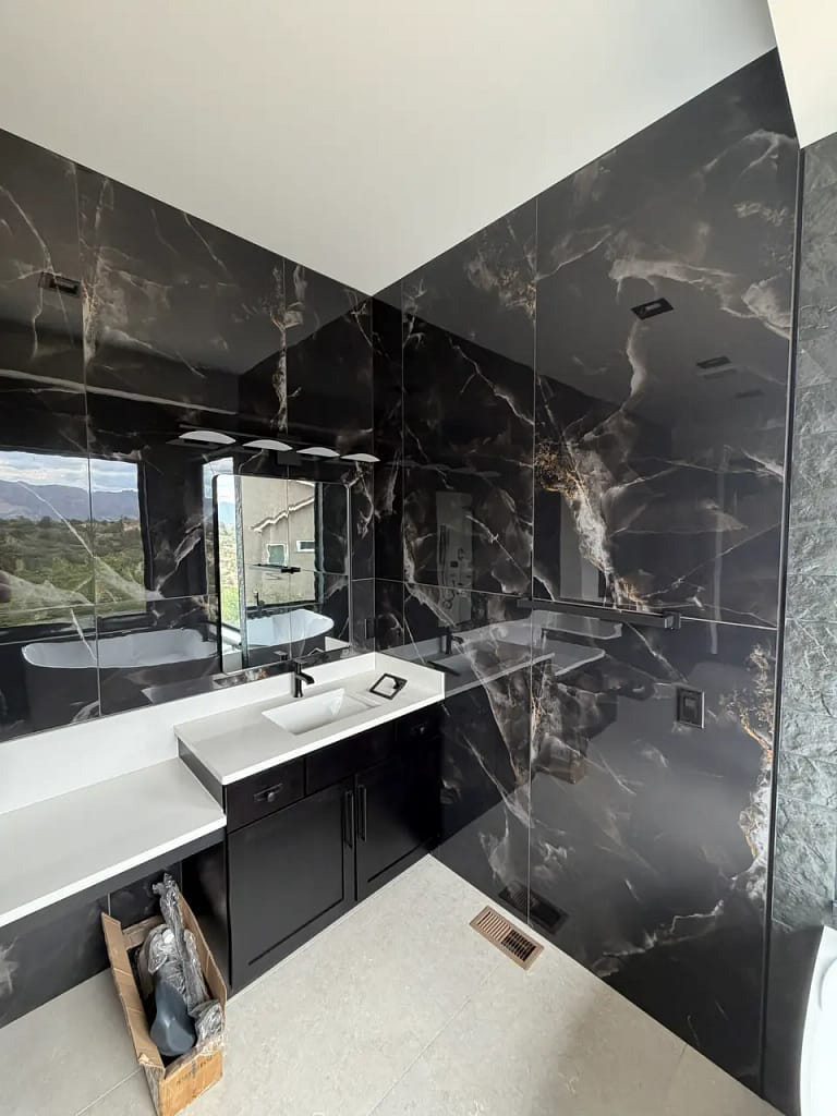 Luxury bathroom featuring full-height dark marble-look gauged porcelain wall panels with striking gold veining. XCEL TILE - Custom Tile Services Colorado Springs