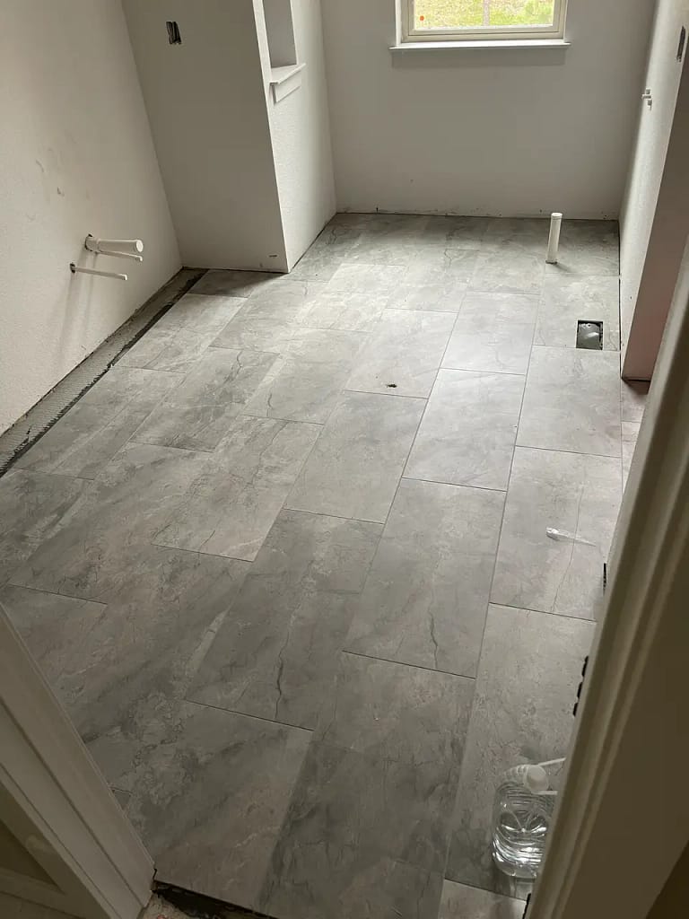 Continuous large-format grey stone-look tile flooring installed seamlessly throughout a residential bathroom and water closet in Monument, CO, by XCEL TILE.
