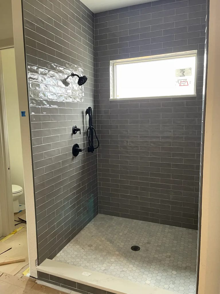 Finished custom walk-in shower in Larkspur, CO, featuring glossy grey subway tile walls, a white marble hexagon mosaic floor pan, and modern matte black fixtures by XCEL TILE.